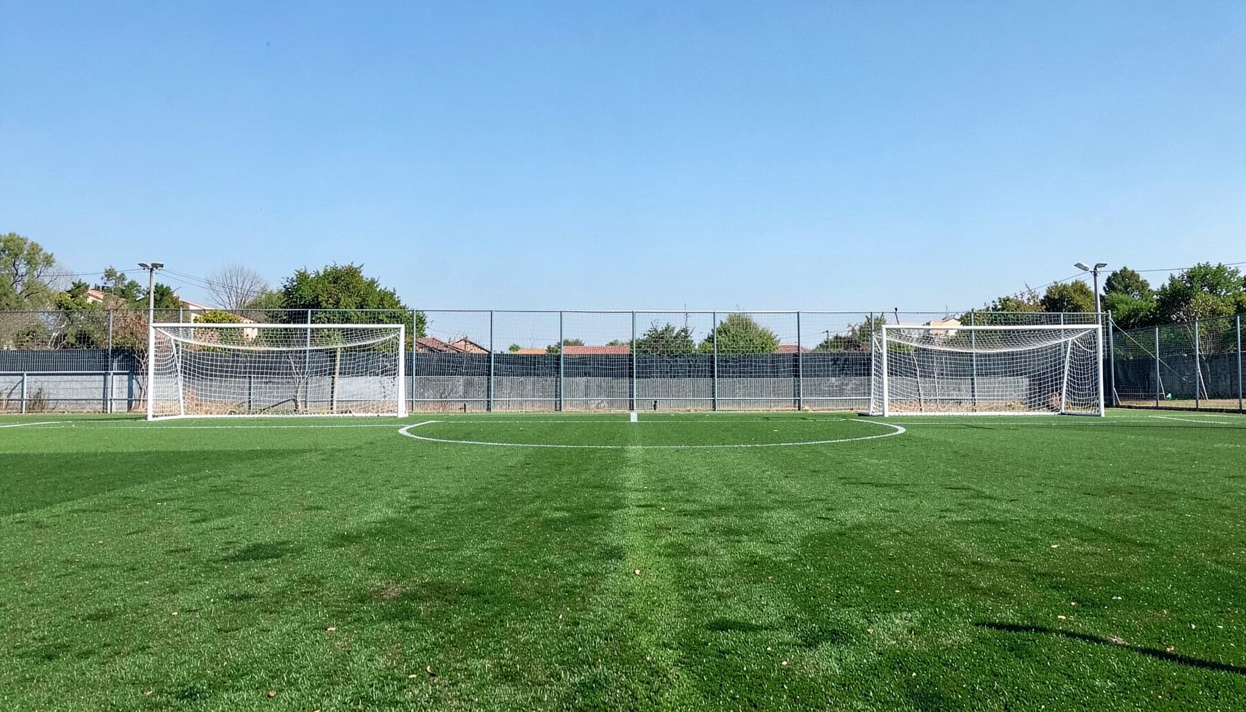Campo de fútbol con césped verde y arcos blancos bajo cielo despejado