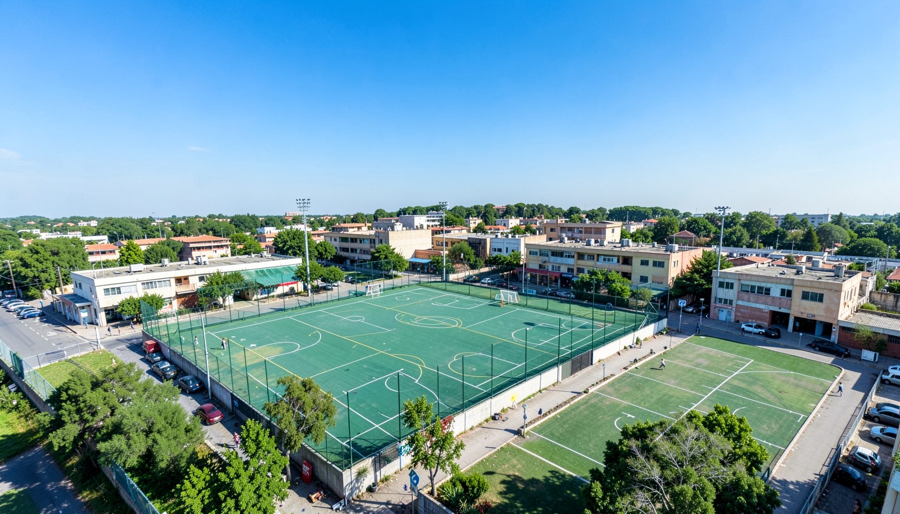 Vista aérea de la Villa Deportiva del club con canchas al aire libre y edificios bajos, bajo un cielo azul despejado, en tonos verdes y celestes