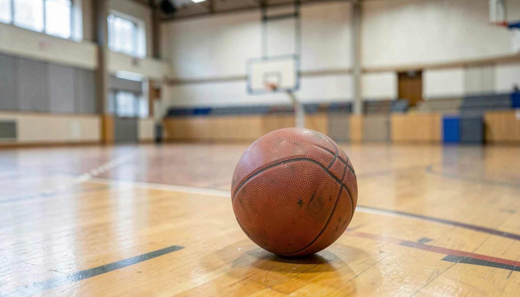 Cancha de básquet con una pelota en primer plano, iluminación suave de gimnasio, ambiente sereno y deportivo