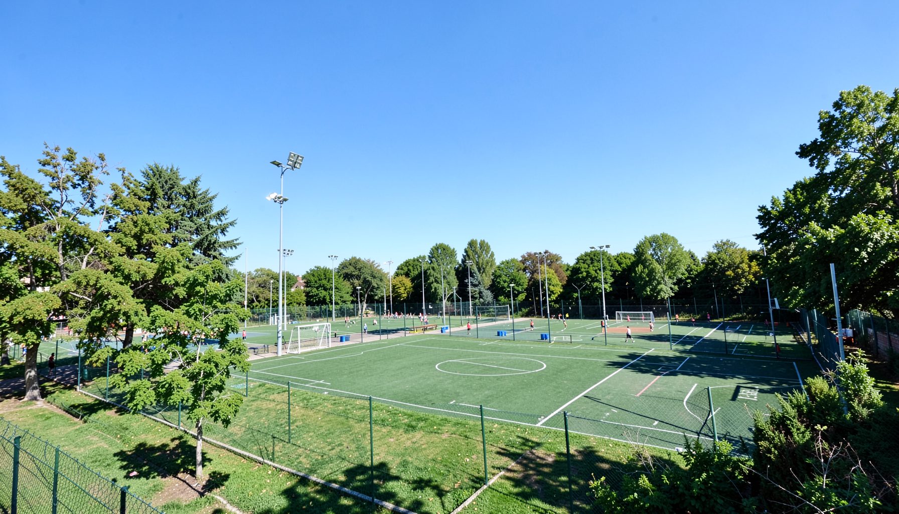 Vista amplia de la Villa Deportiva del club en un día soleado, con canchas al aire libre rodeadas de árboles y el cielo celeste claro, transmitiendo amplitud y espíritu deportivo familiar.