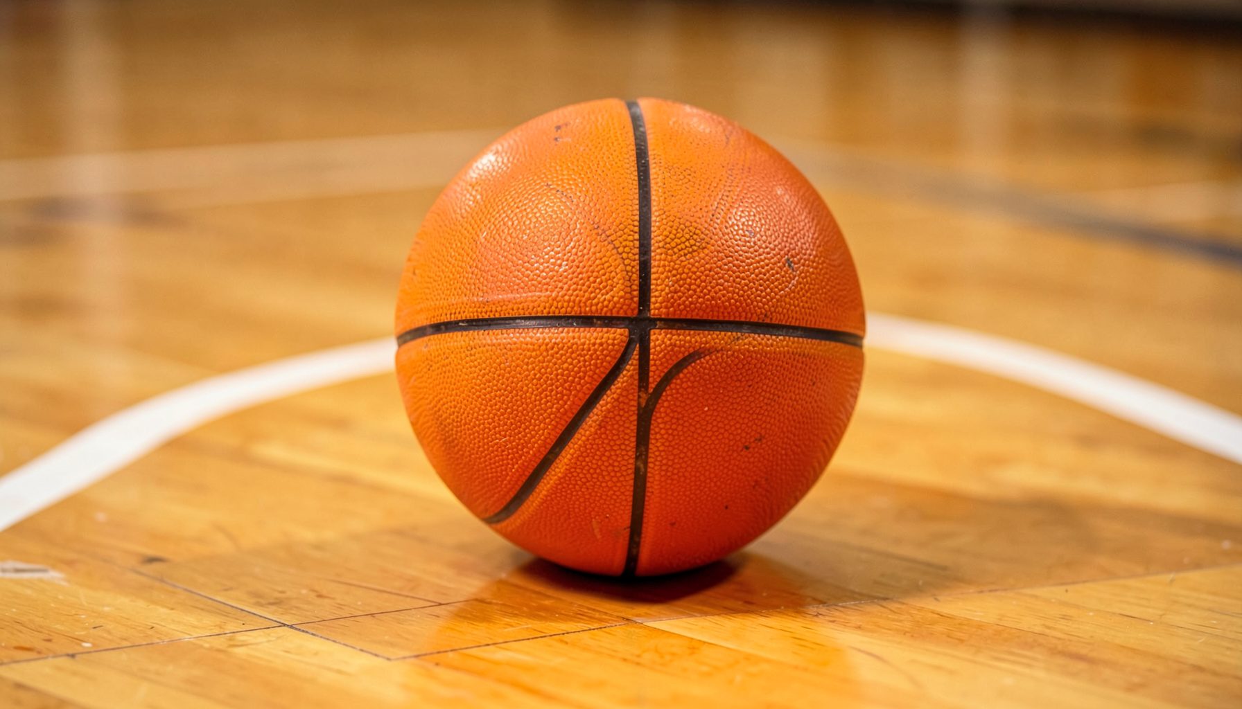 Pelota de básquet naranja sobre una cancha de madera con líneas blancas, iluminación cálida