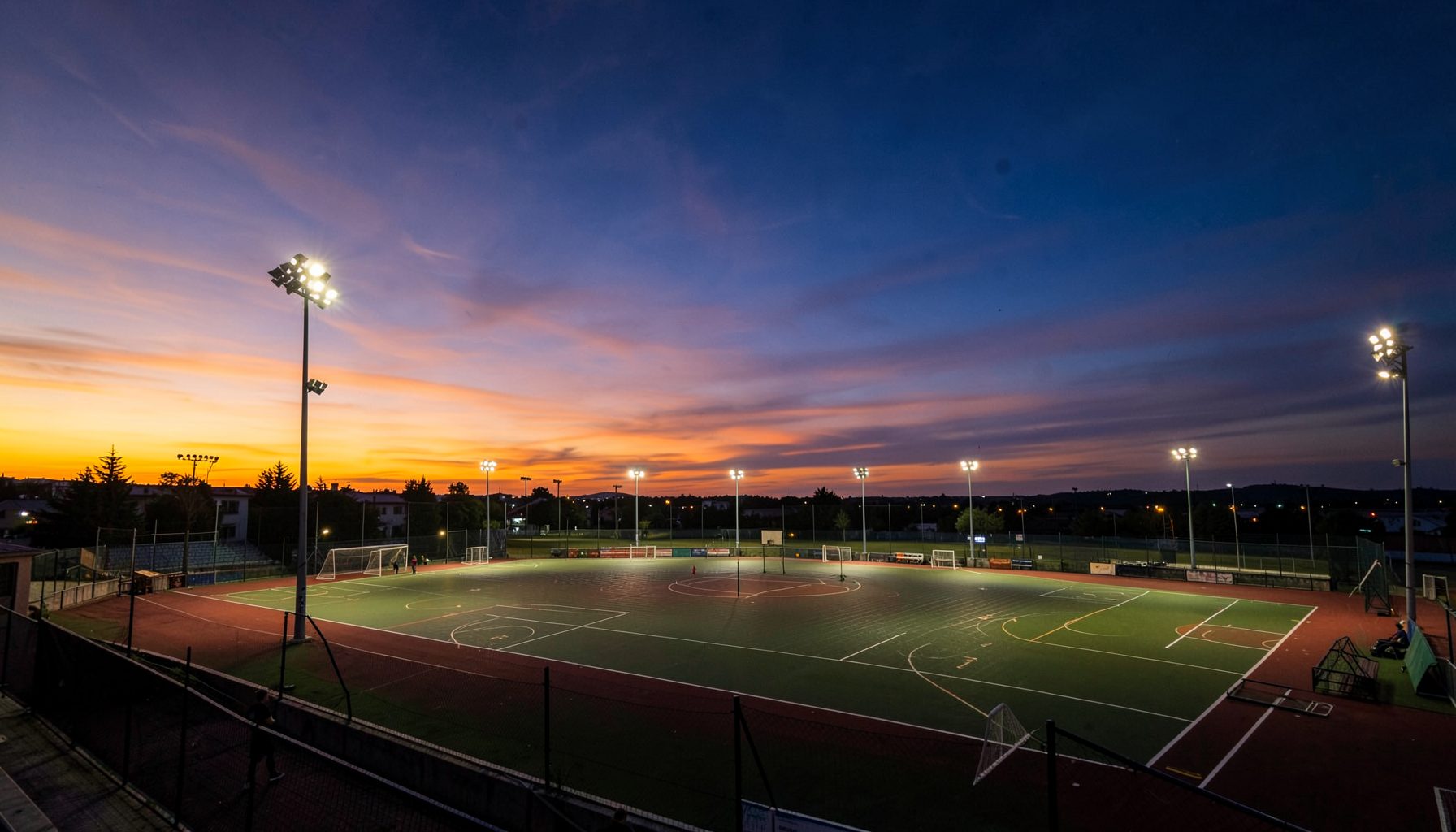Vista panorámica de la Villa Deportiva del club al atardecer, con canchas iluminadas y un cielo en tonos anaranjados y azules profundos
